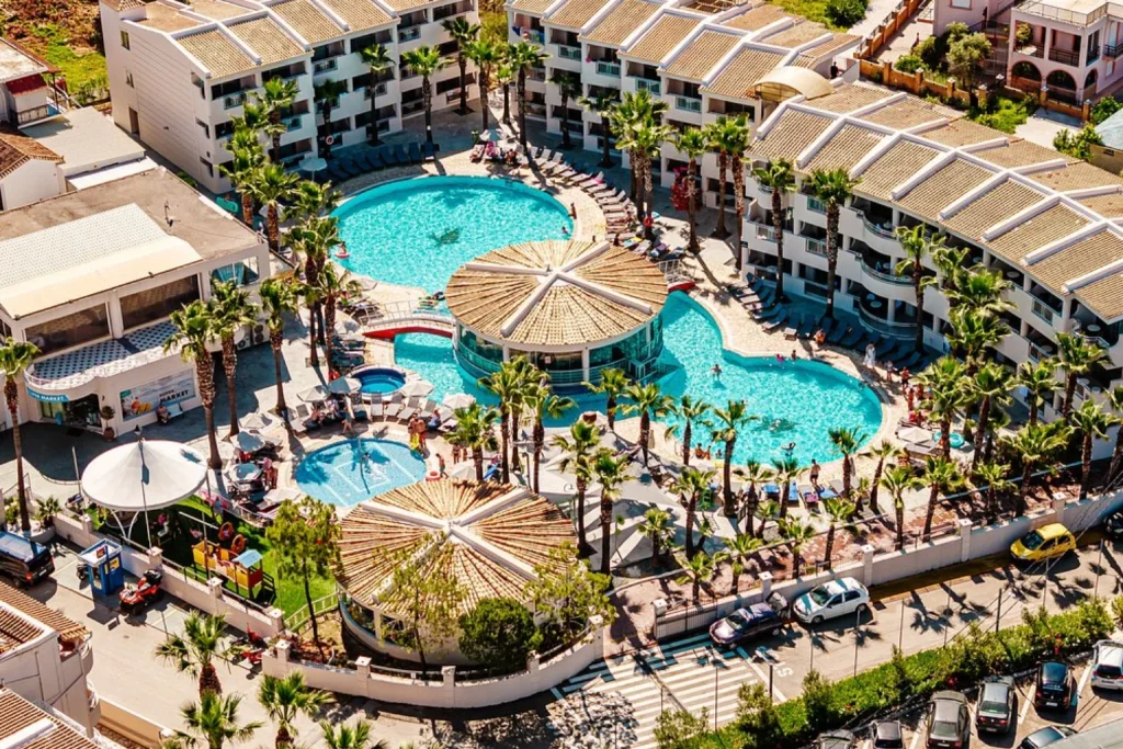 Aerial view of large swimming pools, palm trees and surrounding resort buildings at Caretta Beach Resort & WaterPark, Zakynthos