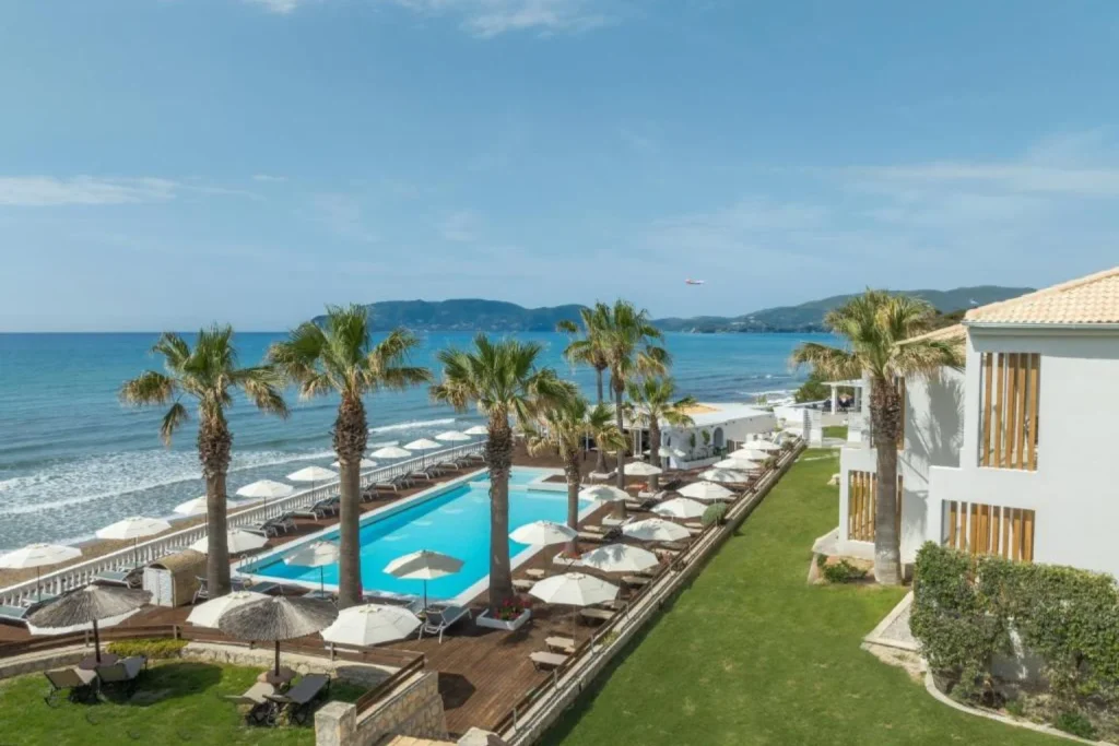 Beachfront swimming pool with palm trees and panoramic Ionian Sea views at Crystal Beach Hotel, Zakynthos